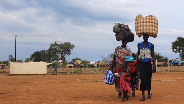 Des femmes avec des ballots sur la tête marchent à côté de trois jeunes enfants