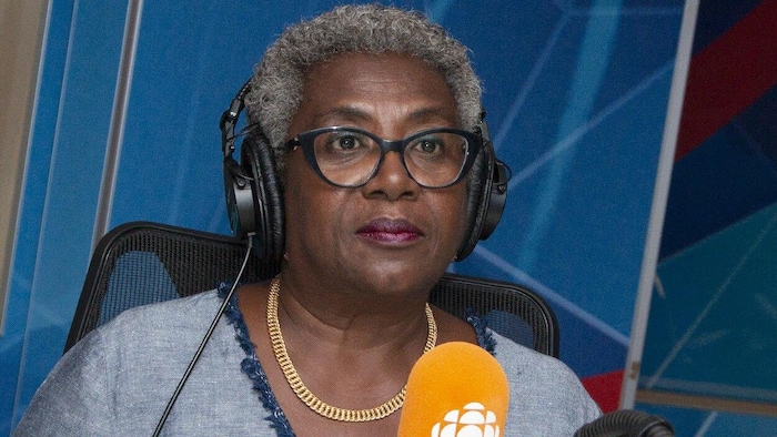 Régine Laurent est assise devant un micro de radio et porte un casque d'écoute sur la tête.