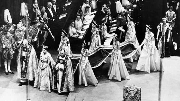 La reine Élisabeth II suivie par six femmes tenant la traîne de sa robe lors de son couronnement à l'abbaye de Westminster.