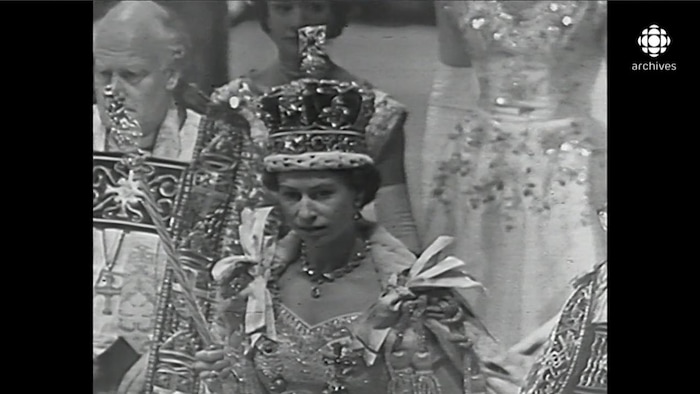 La reine Élisabeth II, sceptre à la main avec sa lourde couronne sur la tête, en procession à la suite de son couronnement.
