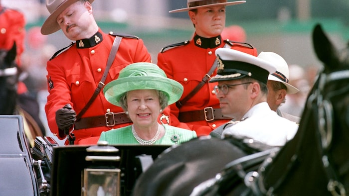 La reine Élisabeth II, à bord d'une calèche, est entourée d'agents de la Gendarmerie royale du Canada.