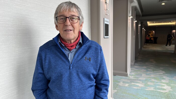 Un homme habillé en bleu est debout dans un couloir dont le plancher est couvert d'un tapis turquoise.