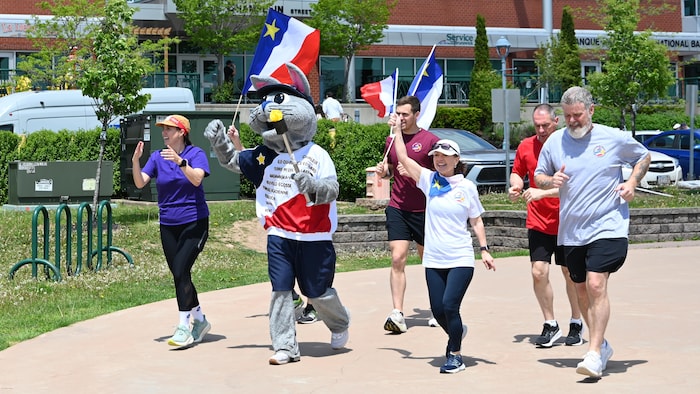 Cinq adultes courent avec la mascotte des Jeux. 