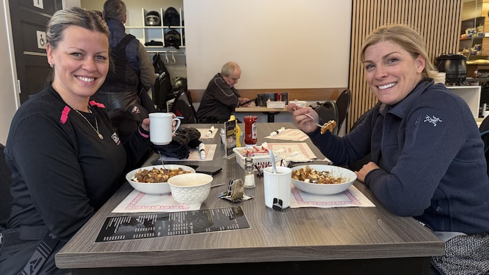 Deux femmes assises à une table de restaurant avec des poutines.