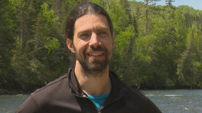 Gros plan sur le visage de Rémi Lesmerises, debout devant une rivière.