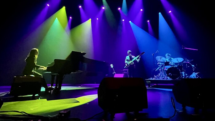 Une scène illuminée où se produisent des artistes musicaux, tels une pianiste, un guitariste et un batteur.