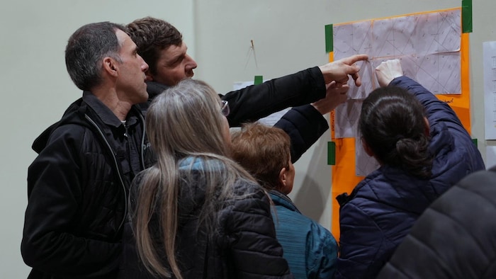 Des citoyens regardent une feuille sur laquelle est cartographiée les claims de l’entreprise Richmond Hill Ressources en lien avec le projet minier.