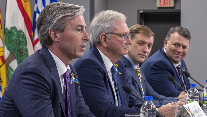 Les quatre premiers ministres sont assis en rang à une longue table. Tim Houston, complètement à gauche, s'adresse au public.