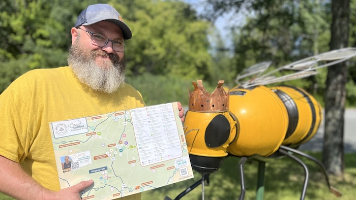 Un homme habillé de jaune tient une carte à côté d'une abeille géante.