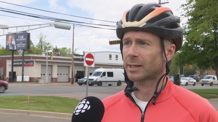 Un homme en vélo, portant un casque, en entrevue.