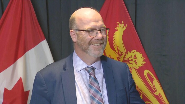 René Legacy, souriant, devant un drapeau du Nouveau-Brunswick.