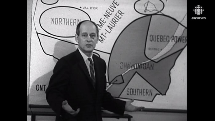 René Lévesque gesticule devant une carte du Québec.
