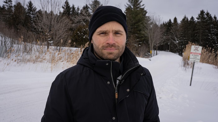 Un homme avec un manteau d'hiver noir et une tuque devant un sentier de motoneige.
