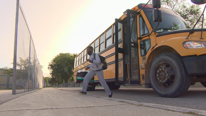Un élève quitte un autobus scolaire pour se rendre dans une cour d'école dans la lumière du matin.