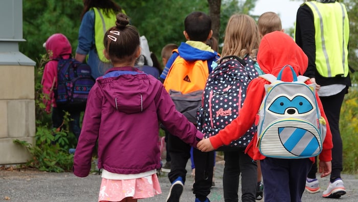 Photo d'enfants qui se tiennent la main en marchant vers l'entrée de leur école avec leurs sacs à dos.