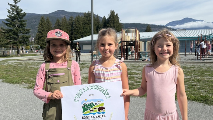 Trois filles devant une école, des arbres et des montagnes.