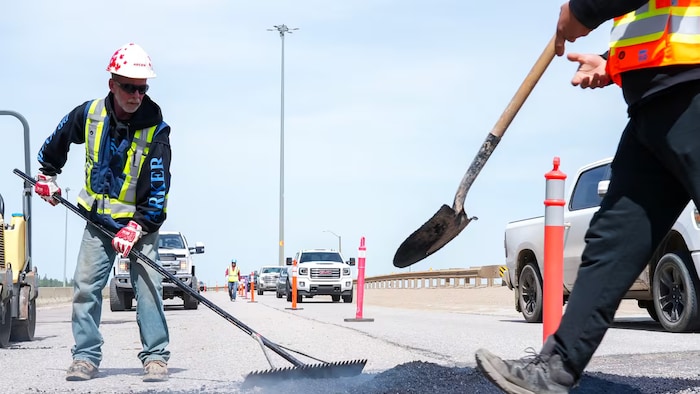 Des bénévoles comblent des nids-de-poule sur un tronçon de l'autoroute 63 qui longe le centre-ville de Fort McMurray, le 12 juin 2026.