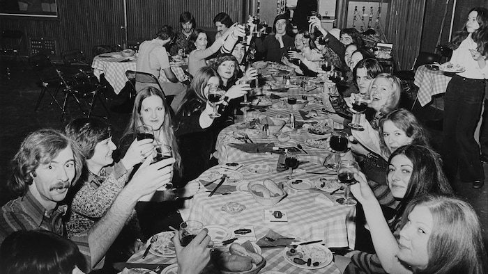 Guides, hôtesses et autres membres du personnel des relations publiques de Radio-Canada attablés à une longue table devant un repas traditionnel des Fêtes.