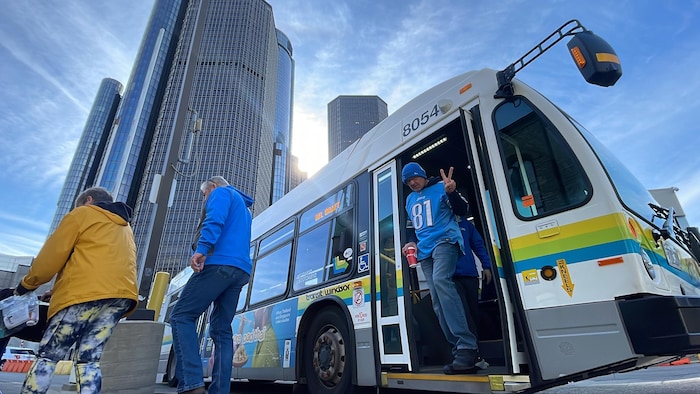 Un partisan habillé avec un chandail d'une équipe de la NFL fait un signe de paix en débarquant d'un autobus municipal de Windsor arrêté à Détroit.