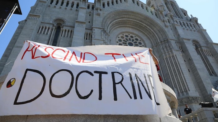 Dos indígenas sostienen una pancarta pidiendo el fin de la Doctrina del Descubrimiento.