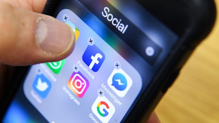 Un homme tient un téléphone intelligent avec les icônes des applications de réseaux sociaux Facebook, Instagram et Twitter.
