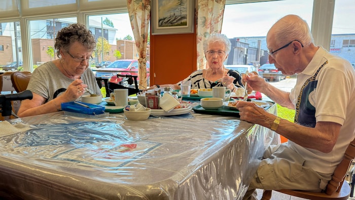 Trois aînés mangent autour d'une table. 