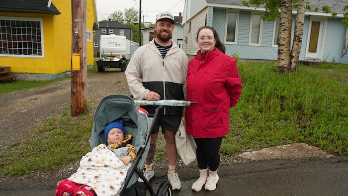 Un couple avec un bébé dans une poussette, devant une maison.