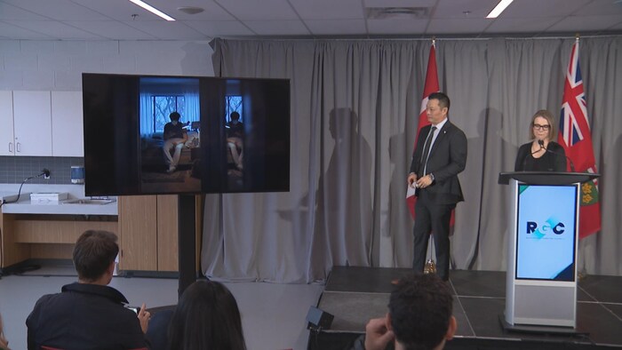 Stan Cho et Sarah McCarthy pendant une conférence de presse présentant une vidéo devant une salle.