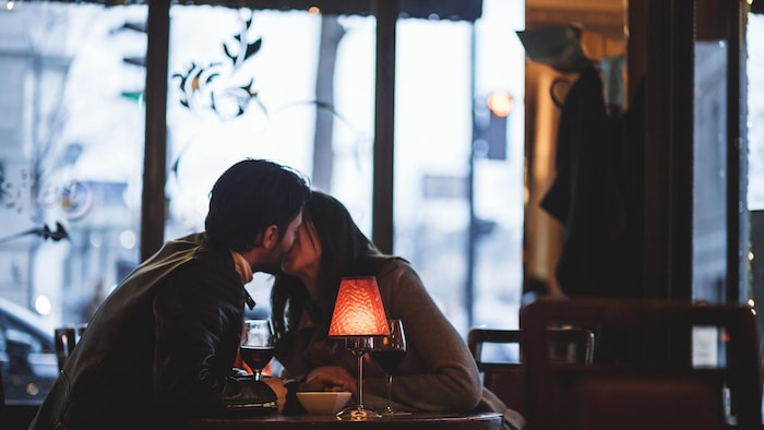 Deux amoureux s'embrassent dans un restaurant de la ville avec la lumière tamisée. 