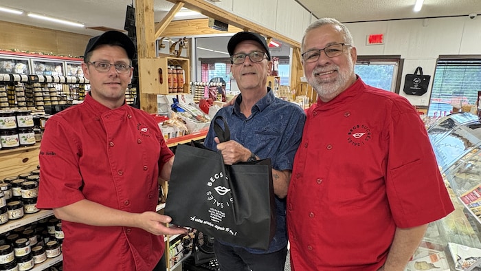Dans une boutique, Marc Lacroix, Régis Helin et Yves Moreau tiennent un sac destiné à des sinistrés.