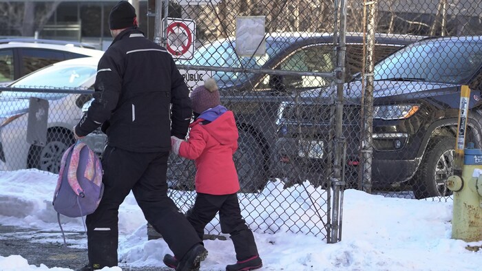 Un homme tient une fillette par la main et transporte son sac d'école.