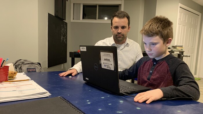 Le père supervise son fils qui est devant un ordinateur portable pour suivre ses cours en ligne depuis chez lui 