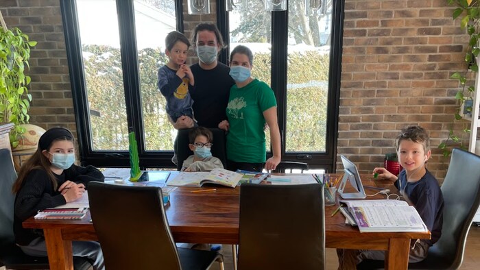 Une famille composée de deux parents et de quatre enfants installée autour d'une table. Plusieurs portent un masque.