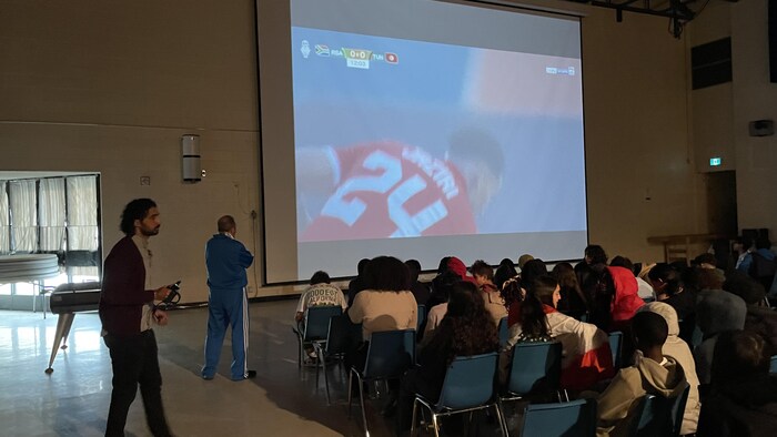 Des élèves de dos qui regardent une retransmission d'un match de soccier de la Coupe d'Afrique des Nations.