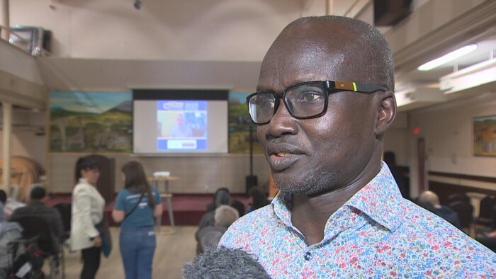 Reuben Garang debout dans une salle où on aperçoit des gens de façon floutée le 12 avril 2025 à Winnipeg.