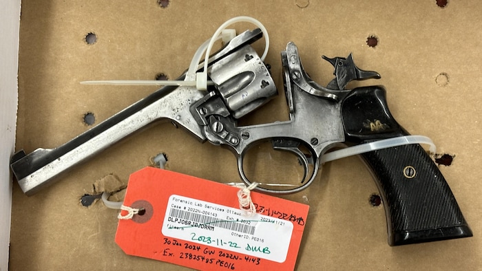 Un revolver attaché à une boîte de carton. Une étiquette orange est attachée à l'arme. 