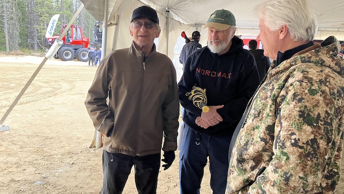 Richard Desjardins et Henri Jacob observent quelque chose sous un chapiteau en discutant avec un homme.