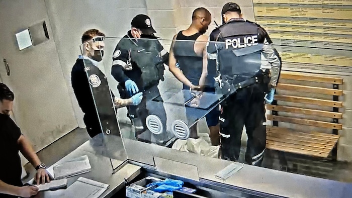 Richard Edwin en caleçon et en débardeur entouré de policiers.