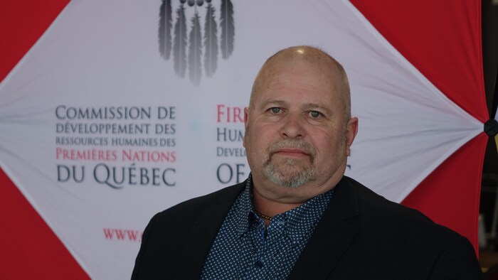 Richard Jalbert photographié devant une banderole où il est inscrit Commission de développement des ressources humaines des Premières Nations du Québec.