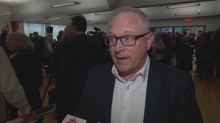 Richard Losier en entrevue dans une salle bondée de gens.