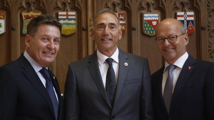 Trois hommes côte à côte sourient à la caméra.
