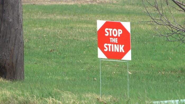 Un écriteau carré planté sur le gazon. Il représente un octogone rouge dans lesquels les mots « Stop the Stink » sont écrits en lettres blanches.
