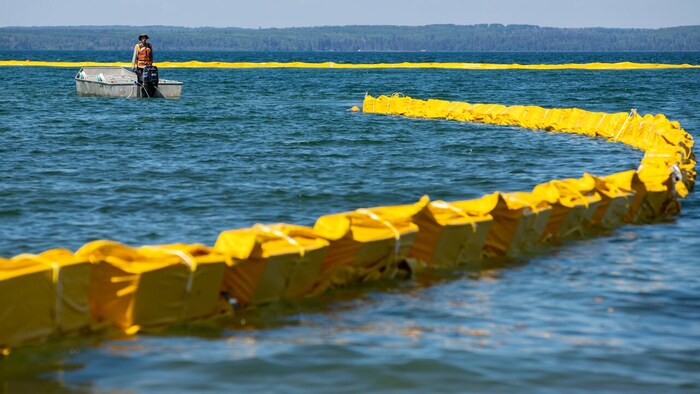 Un homme est debout sur son bateau pour superviser le déploiement du rideau de confinement.