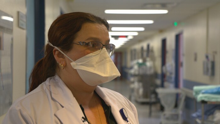 Une femme portant un masque et des lunettes dans un corridor d'hôpital.
