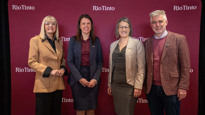 Trois femmes et un homme prennent la pose devant le logo de l'entreprise aluminière Rio Tinto.