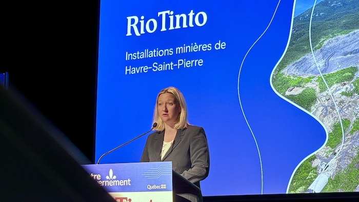 Une femme parle au micro devant un écran géant.