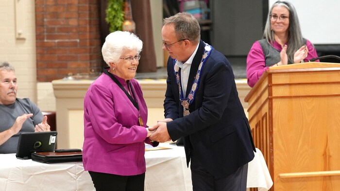 Une femme reçoit sa médaille du maire.