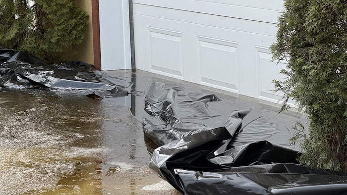 L'eau d'un lac à Rouyn-Noranda a monté jusqu'à la porte d'un garage. Une bâche a été déployée pour empêcher l'eau de rentrer.