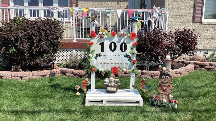 Une maison arborant fièrement une pancarte artisanale marquée du chiffre « 100 » et du nom de la municipalité de Rivière-au-Tonnerre.