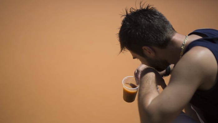 Un homme remplit une tasse d'eau dans la rivière boueuse. 

